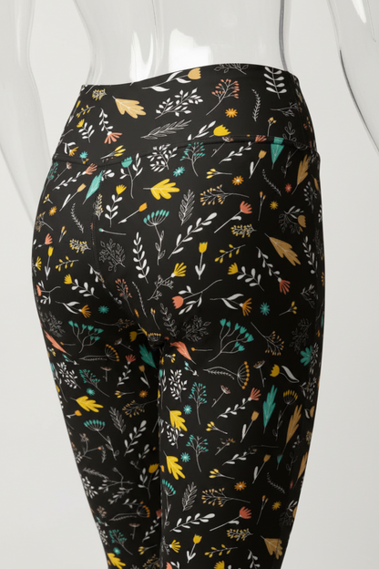 Close-up of a mannequin wearing black leggings with a colorful botanical and floral print, showing the hip and thigh area against a plain white background.