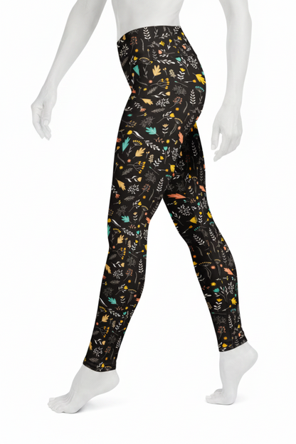 A mannequin wearing high-waisted leggings with a black background and a colorful, playful pattern of birds, leaves, and abstract shapes in yellow, teal, orange, and white.