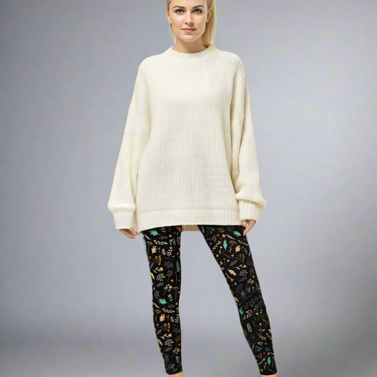 Model wearing Harvest Sky Yoga Leggings with black base and nature-inspired print in orange, teal, yellow, and white, styled with an oversized cream ribbed sweater and brown slip-on shoes; casual everyday look blending comfort with country-inspired activewear.