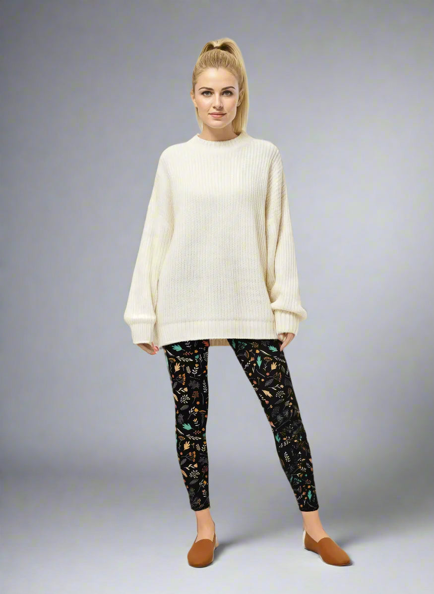 Model wearing Harvest Sky Yoga Leggings with black base and nature-inspired print in orange, teal, yellow, and white, styled with an oversized cream ribbed sweater and brown slip-on shoes; casual everyday look blending comfort with country-inspired activewear.