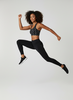 Woman in black athletic wear jumping in the air against a white background