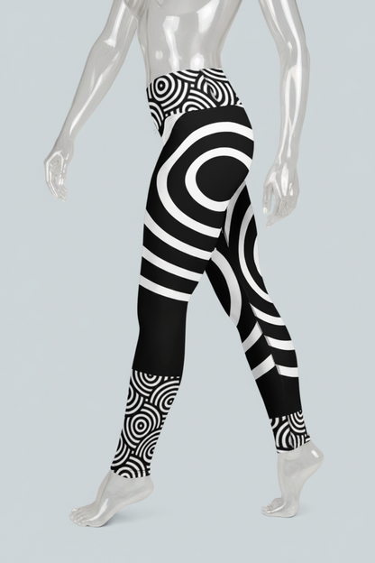 Black and white high-waisted leggings with a bold concentric circle and spiral pattern, shown on a model from the waist down against a light gray background.