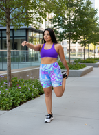 Woman in athletic wear stretching outdoors on a sidewalk with trees and buildings in the background
