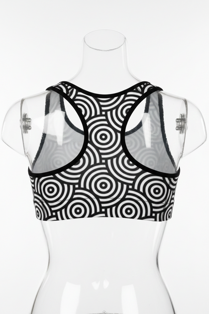 A black and white cropped tank top with a bold concentric circle target pattern and contrasting white shoulder panels, shown against a plain white background. 