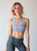 Woman wearing a colorful sports bra and dark leggings against a plain background