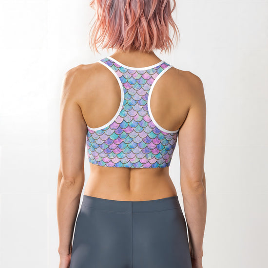 Woman showing the back of the Lumina Siren Essential Active Bra with a pastel blue, purple, and pink mermaid scale pattern, standing against a plain background