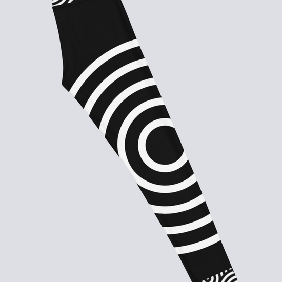 Right‑side view of black high‑waisted Lunar Loops yoga leggings with bold white concentric circle pattern, featuring large circular motif on thigh and smaller circles near waistband and ankle for a striking, modern look.