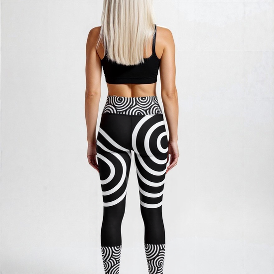 Back view of a woman wearing Lunar Loops Yoga leggings with striking black and white concentric circle print and a black sports bra, standing against a plain light background.