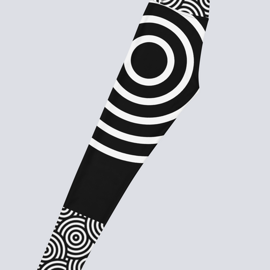 Left‑side view of black high‑waisted Lunar Loops yoga leggings with bold white concentric circle pattern, featuring large circular motif at mid‑thigh and smaller circles near waistband and ankle for a striking, modern look.