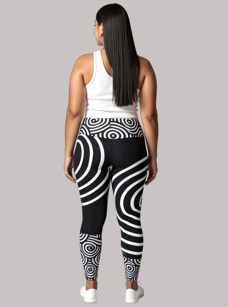 Back view of a model wearing Pixie & Sherbet’s Lunar Loops leggings with bold black and white concentric circle patterns, paired with a white sleeveless top and white sneakers, standing against a light background in a relaxed, upright pose.
