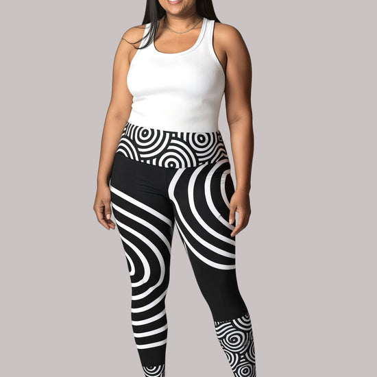 Model smiling in Pixie & Sherbet’s Lunar Loops leggings featuring bold black and white concentric circle patterns, paired with a white sleeveless top and white sneakers, standing confidently against a light background.
