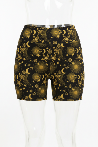 Black yoga shorts with a gold celestial pattern of stars, moons, and sunbursts, shown on a model.