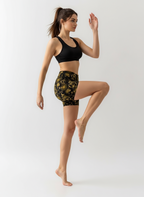 Woman wearing black sports bra and gold floral shorts on a white background