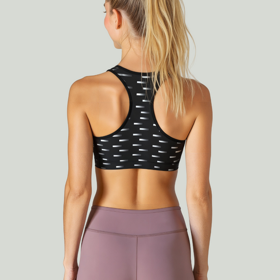 Woman wearing a black sports bra with white patterns and pink leggings against a plain background