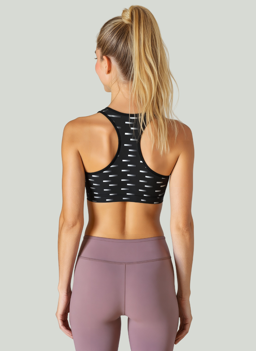 Woman wearing a black sports bra with white patterns and pink leggings against a plain background