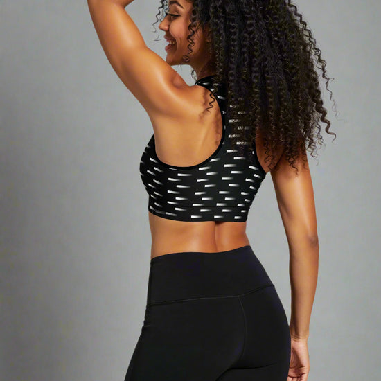 Back view of woman wearing Nightfall Edit Essential Active Bra with a black base and white dash print, smiling and showing the racerback design against a plain background