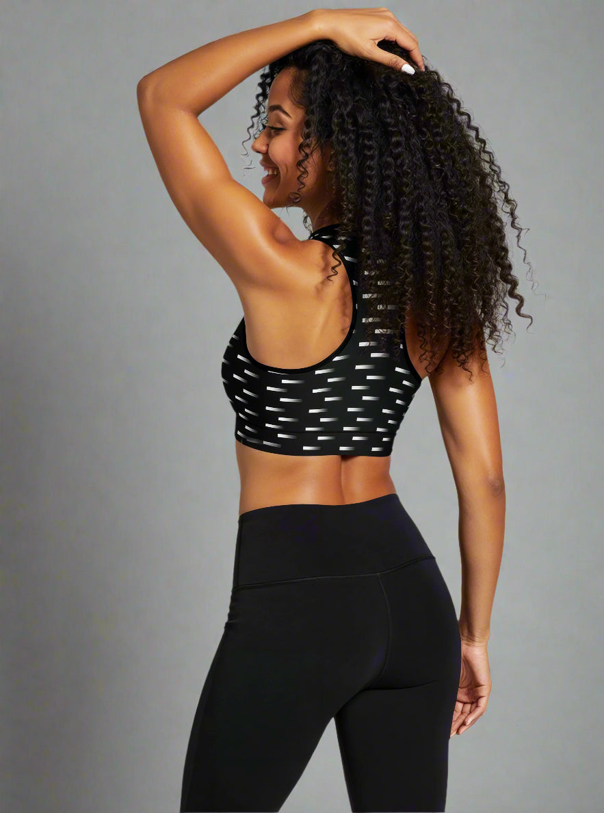 Back view of woman wearing Nightfall Edit Essential Active Bra with a black base and white dash print, smiling and showing the racerback design against a plain background