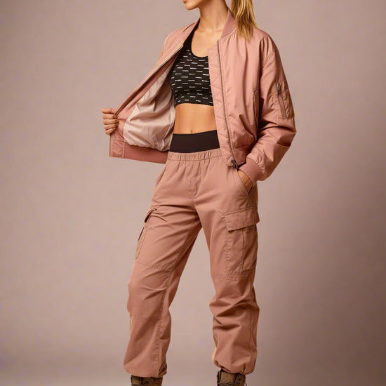 Woman wearing a pink bomber jacket and cargo pants on a beige background