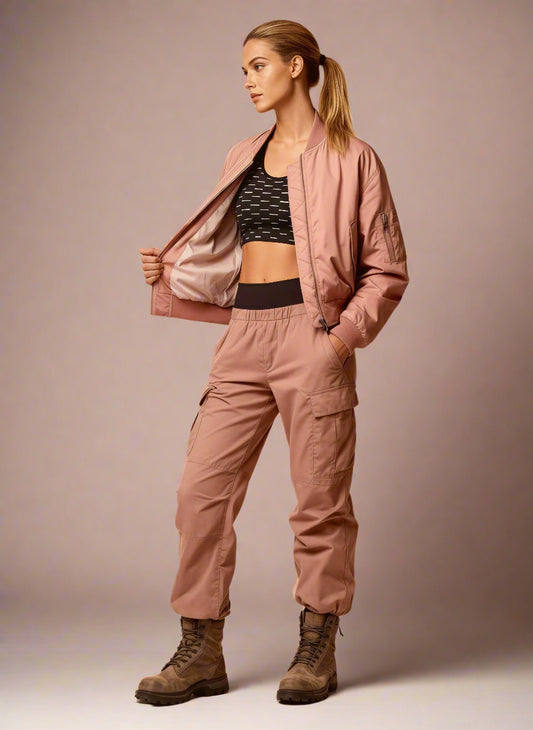Woman wearing a pink bomber jacket and cargo pants on a beige background