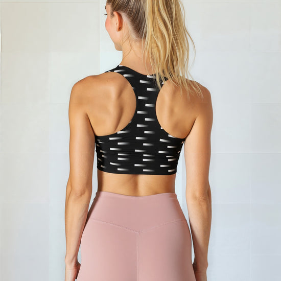 Back view of women wearing the Nightfall Edit longline bra, which features a high-neck design with a black base and a white dash pattern. She pairs the bra with high-waisted mauve leggings, standing against a plain, light background.