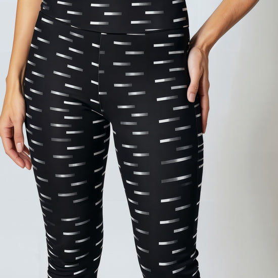 A close-up of a woman wearing Nightfall Edit leggings, showcasing the high-waisted fit and all-over black fabric with a white dash pattern. The image highlights the sleek waistband and the modern geometric print.