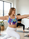 Woman in a colorful sports bra and white leggings stretching in a yoga class.