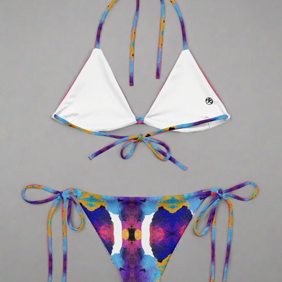 Pixie & Sherbet Ocean Mirage String Bikini, back view laid flat on a neutral background. White triangle cups with multicoloured patterned straps in blue, purple, orange, and yellow, paired with matching tie-side bottoms in the same vivid abstract print. Adjustable fit, premium fabric, and statement-making beachwear style