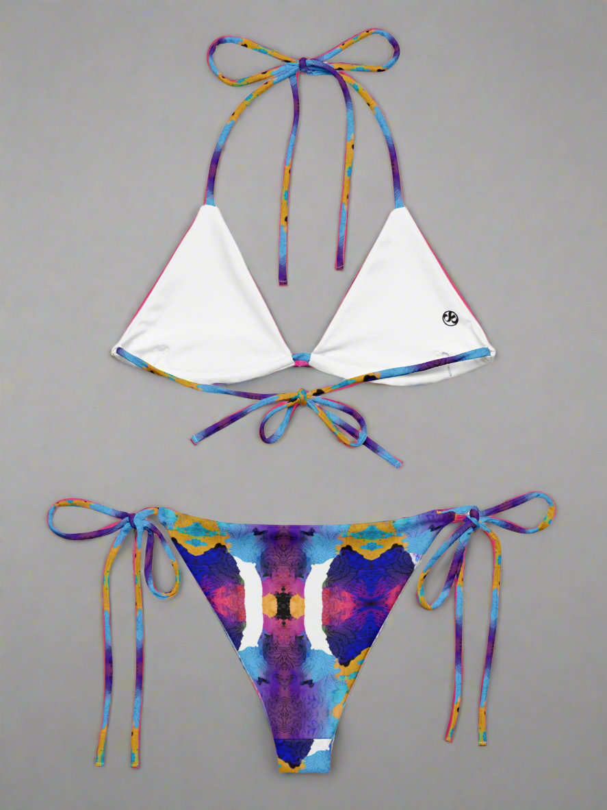 Pixie & Sherbet Ocean Mirage String Bikini, back view laid flat on a neutral background. White triangle cups with multicoloured patterned straps in blue, purple, orange, and yellow, paired with matching tie-side bottoms in the same vivid abstract print. Adjustable fit, premium fabric, and statement-making beachwear style
