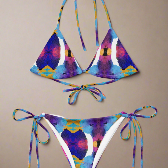 Pixie & Sherbet Ocean Mirage String Bikini, front view laid flat on a neutral background. Classic triangle top and tie-side bottoms in a vibrant, symmetrical abstract print with shades of blue, purple, yellow, and pink. Adjustable neck and back ties, soft stretch fabric, and bold ocean-inspired design for luxe summer swimwear.