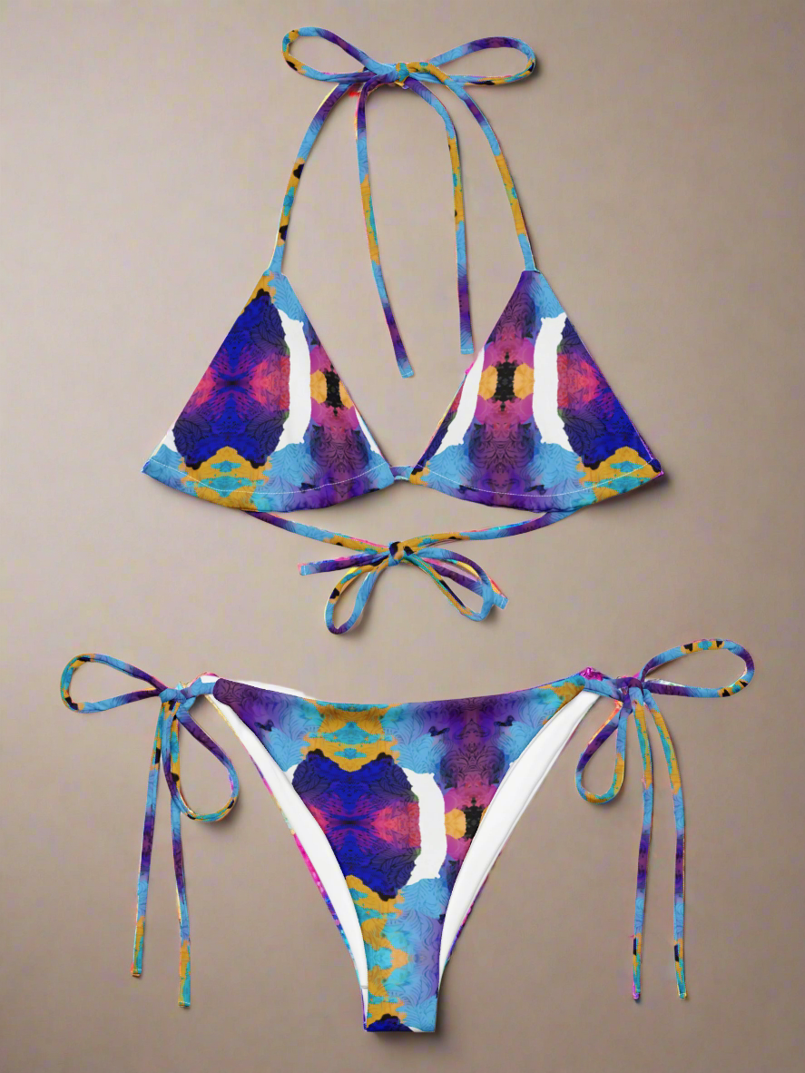 Pixie & Sherbet Ocean Mirage String Bikini, front view laid flat on a neutral background. Classic triangle top and tie-side bottoms in a vibrant, symmetrical abstract print with shades of blue, purple, yellow, and pink. Adjustable neck and back ties, soft stretch fabric, and bold ocean-inspired design for luxe summer swimwear.