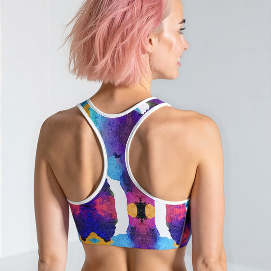 Woman showing the back of the Ocean Mirage Essential Active Bra with a vibrant blue, purple, and yellow abstract print, standing against a plain background