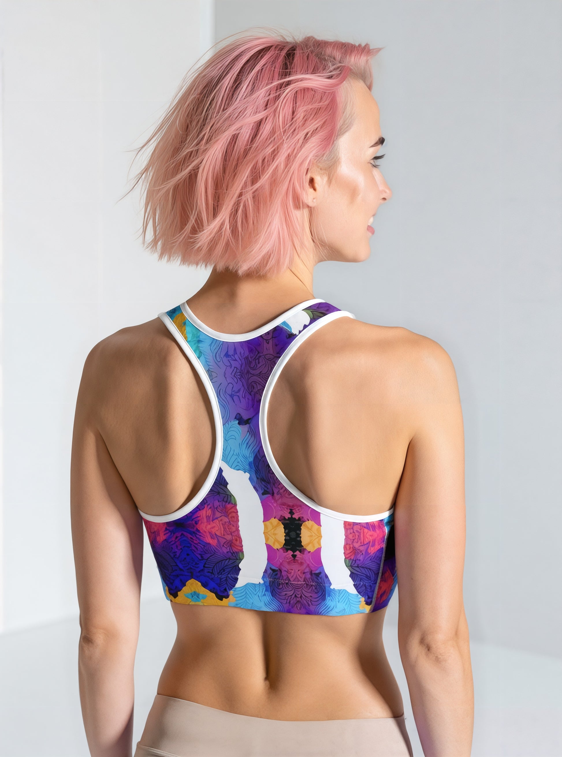 Woman showing the back of the Ocean Mirage Essential Active Bra with a vibrant blue, purple, and yellow abstract print, standing against a plain background
