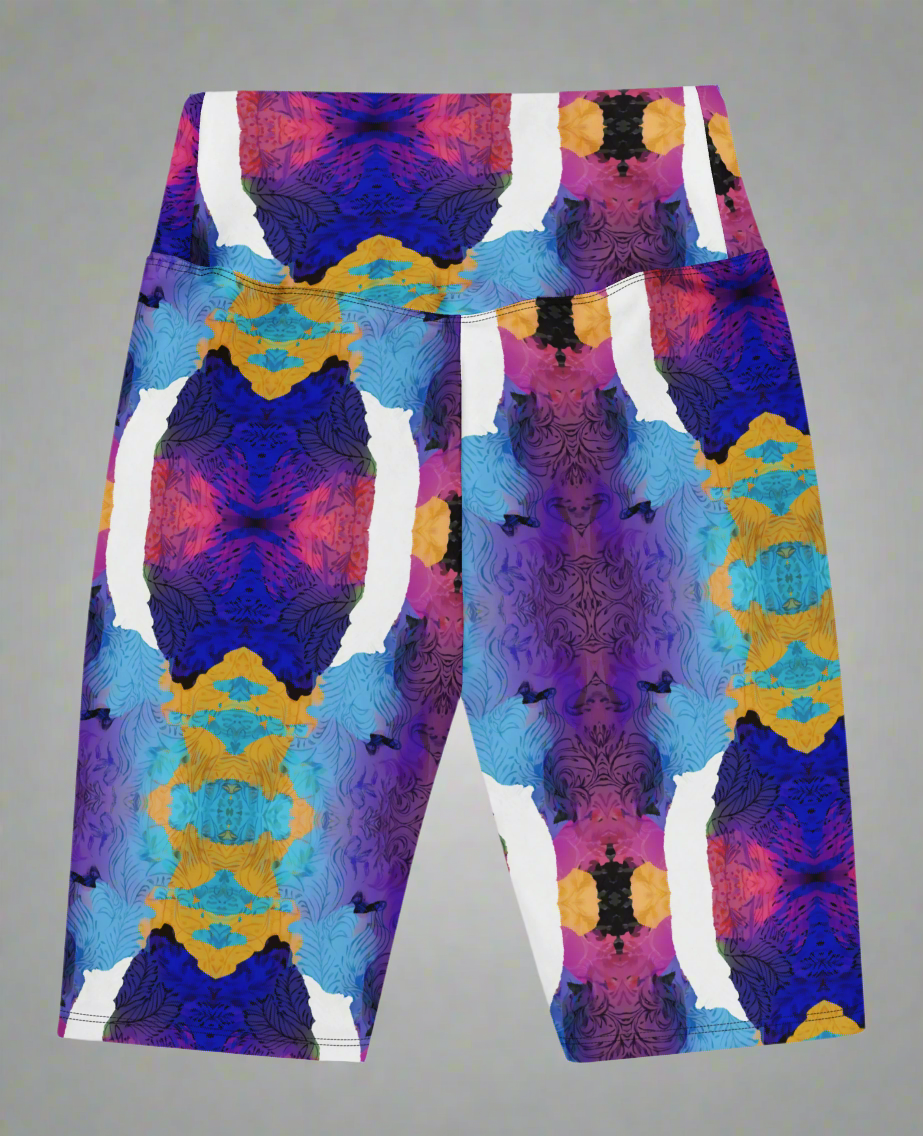 Back view, flat-lay of Ocean Mirage Biker Shorts featuring a vibrant abstract pattern in deep blue, purple, pink, orange, black, and white; displayed flat against a neutral grey background to highlight the bold kaleidoscopic design.