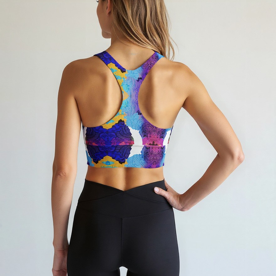 Back view of a woman wearing the Ocean Mirage Longline sports bra, featuring a vibrant and abstract blue, purple, yellow, and white print, paired with high-waisted black leggings, standing against a plain light background.