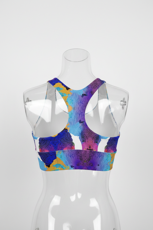 A women's sports bra with a colorful abstract watercolor pattern in purple, blue, and yellow, featuring solid white side panels and a racerback design.