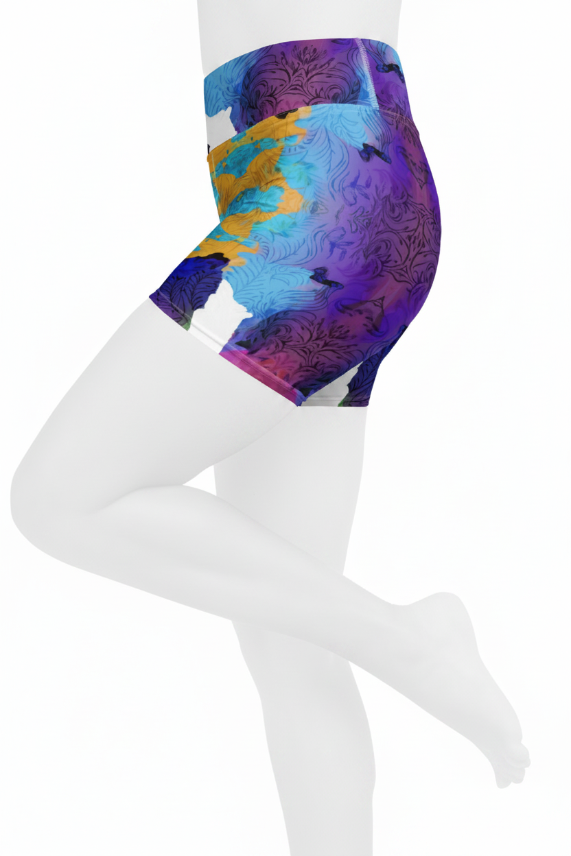 A close-up of a model's lower torso and legs wearing high-waisted athletic shorts with a colorful abstract print in purple, blue, yellow, and white on a plain white background. 