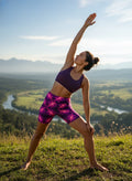 Woman practicing yoga on a grassy hill with a scenic view of a river and mountains.