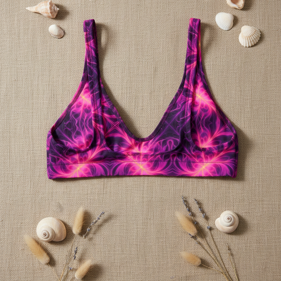 Purple and pink patterned bikini top on a beige fabric background with shells and dried plants.