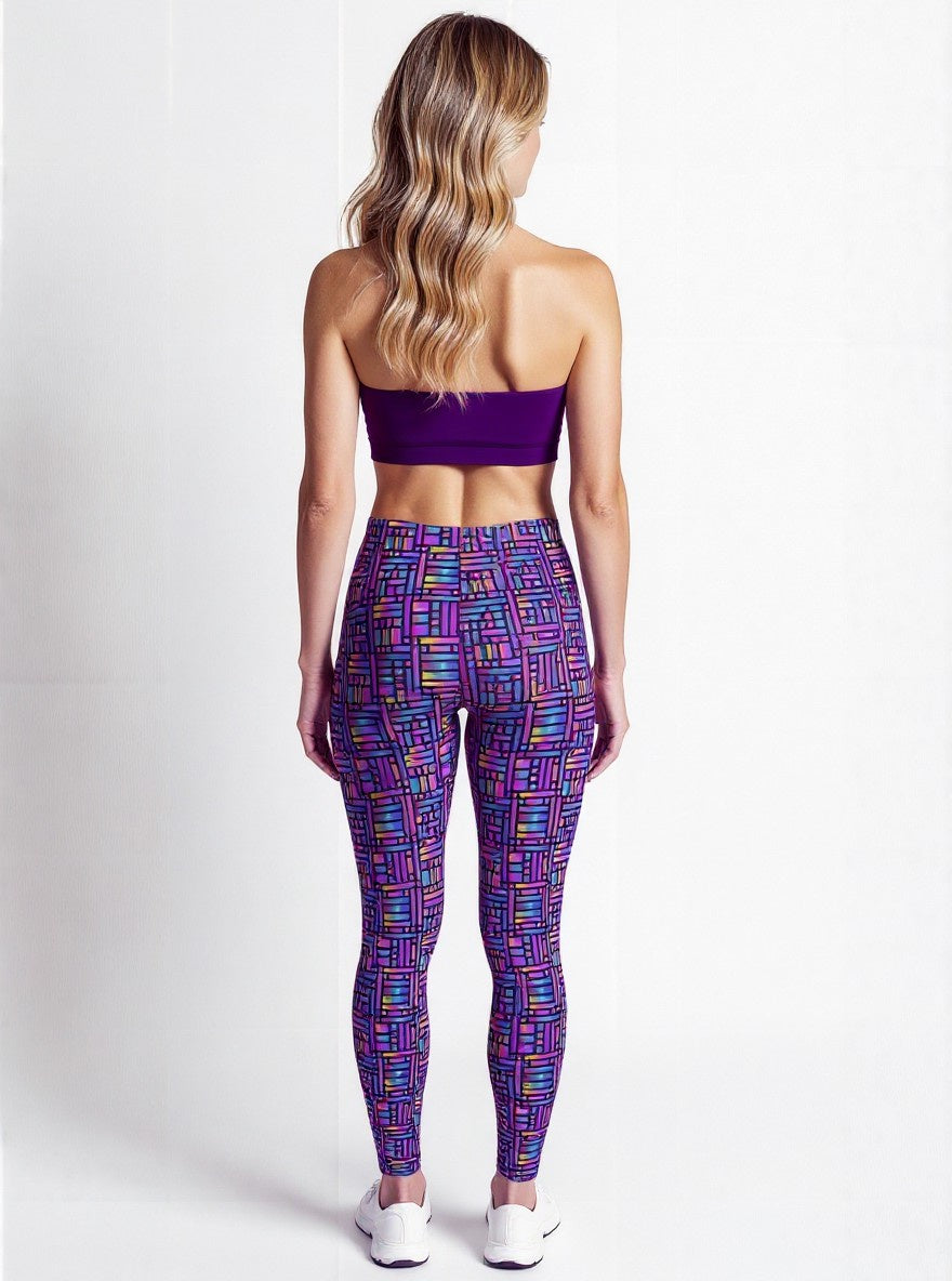 Back view of a woman wearing Pixel Pulse Crossover Leggings with a vibrant geometric pattern in purple, blue, and pink, paired with a purple sports bra and white sneakers, standing against a plain background.