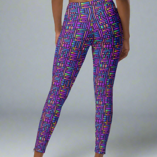 Back view of woman wearing Pixel Pulse Yoga leggings with vibrant multicolored geometric pattern in purple, pink, blue, green, and yellow, paired with a black sports bra, barefoot against a plain gray background.