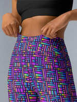 Woman adjusting waistband of Pixel Pulse Yoga leggings with vibrant multicolored geometric pattern in purple, blue, green, and pink, paired with a black crop top, against a neutral background