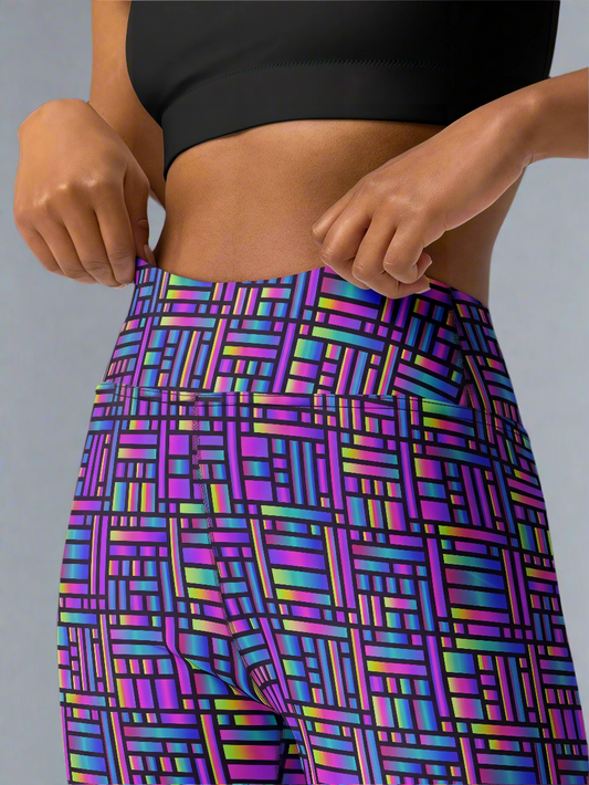 Woman adjusting waistband of Pixel Pulse Yoga leggings with vibrant multicolored geometric pattern in purple, blue, green, and pink, paired with a black crop top, against a neutral background