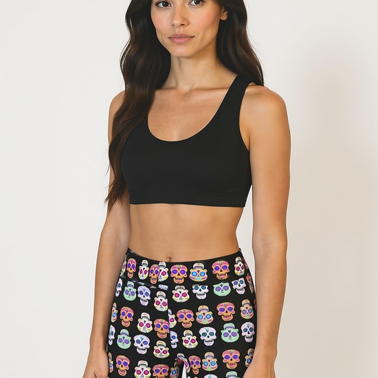 Woman wearing a black sports bra and colourful skull-patterned Pixie and Sherbet Eternal Bloom Yoga Shorts shorts on a plain background