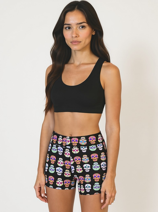 Woman wearing a black sports bra and colourful skull-patterned Pixie and Sherbet Eternal Bloom Yoga Shorts shorts on a plain background