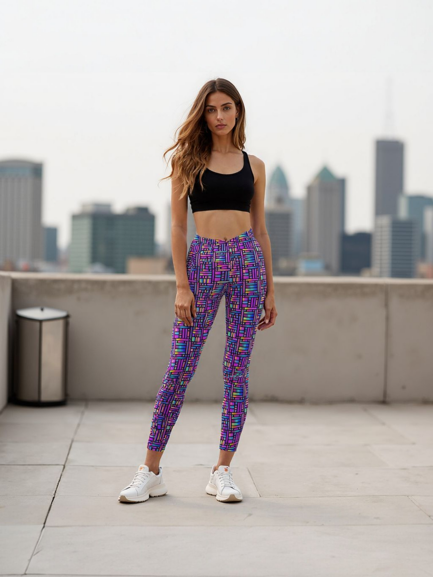 Woman wearing vibrant Pixel Pulse Crossover leggings with a colorful geometric pattern, standing on a rooftop with a city skyline in the background