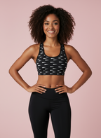 Woman wearing a black sports bra with white patterns and black leggings on a pink background