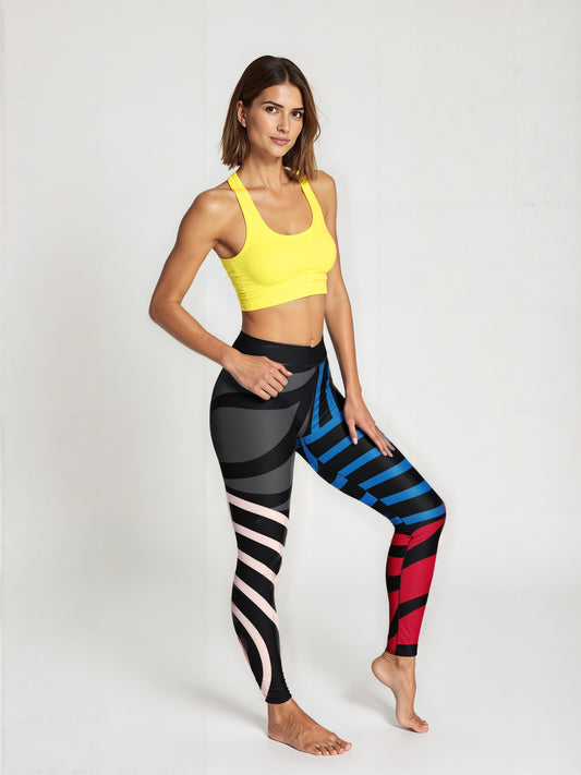 A woman stands barefoot against a plain background, wearing a fitted yellow sports bra and Red, Blue & Onyx Abstract Yoga Leggings. The leggings feature a bold geometric pattern with black, blue, red, and pale pink sections, creating a striking, modern look. The model poses with one hand resting on her hip and one leg slightly bent, highlighting the unique color-blocked design.