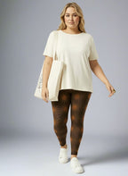 Woman wearing a cream-colored top and patterned leggings with a white bag on a gray background