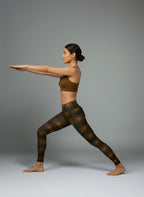 Woman in a yoga pose wearing a brown sports bra and patterned leggings on a gray background