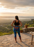 Person wearing colorful leggings and a black tank top standing on a stone patio with a scenic view.